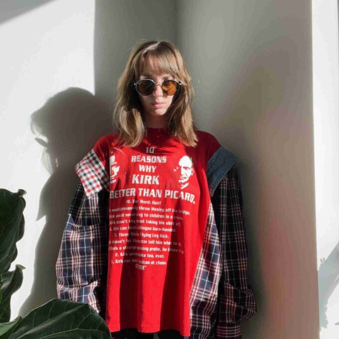 a woman standing against a wall wearing a red shirt.