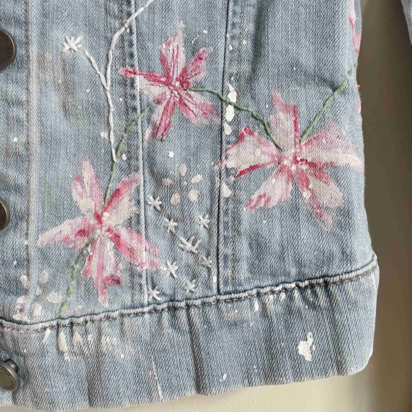 a denim jacket with pink flowers painted on it.