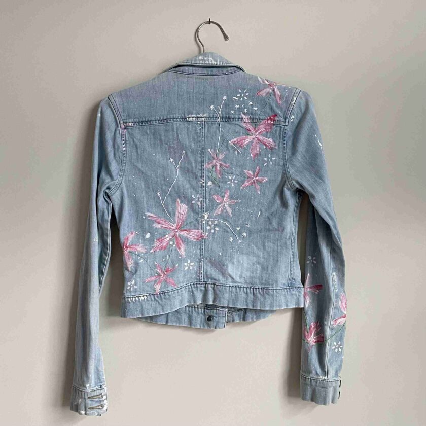 a denim jacket with pink flowers painted on it.