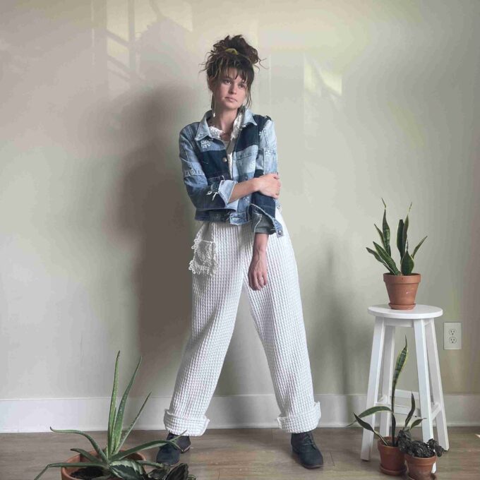 a woman standing in front of a wall next to potted plants.