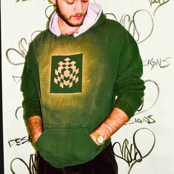 a man in a green hoodie standing in front of a wall.