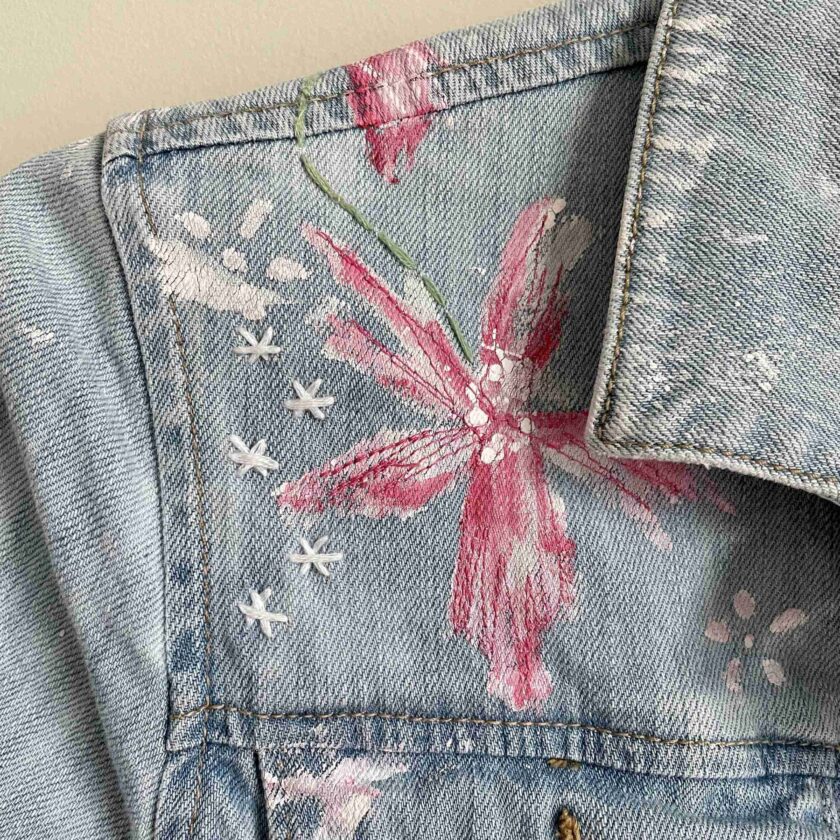 a blue jean jacket with a pink flower on it.