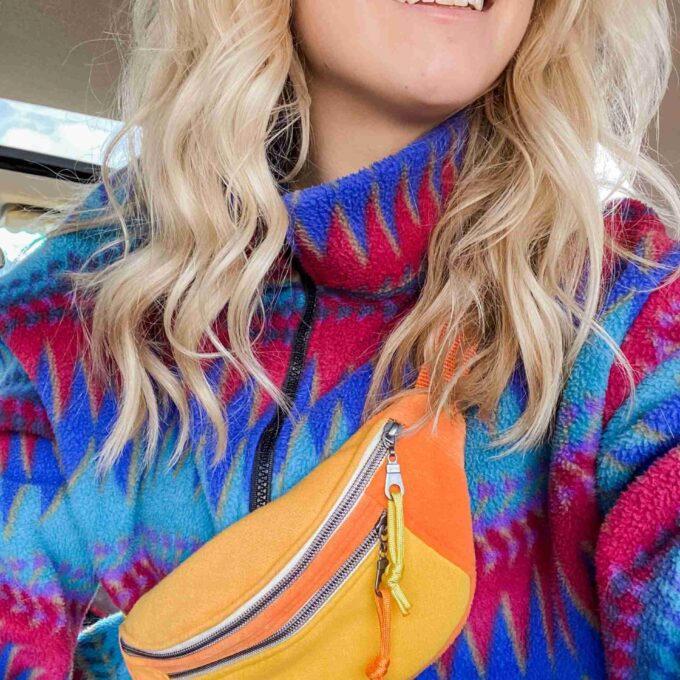 a woman wearing a colorful sweater and pink sunglasses.