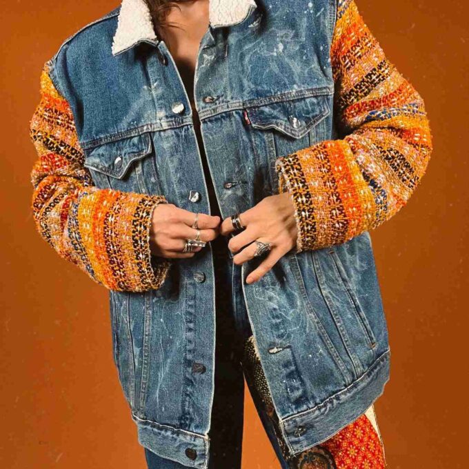 a woman wearing a denim jacket with a multicolored sleeve.