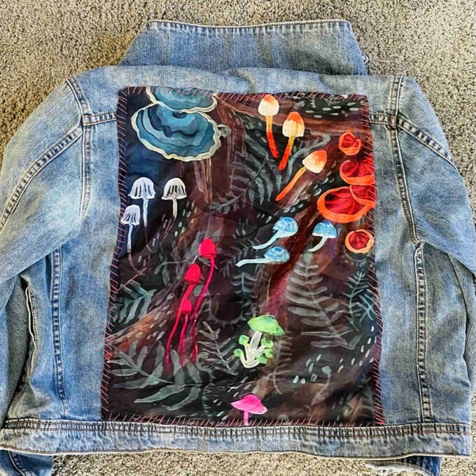 a jean jacket with a painting on the back of it.