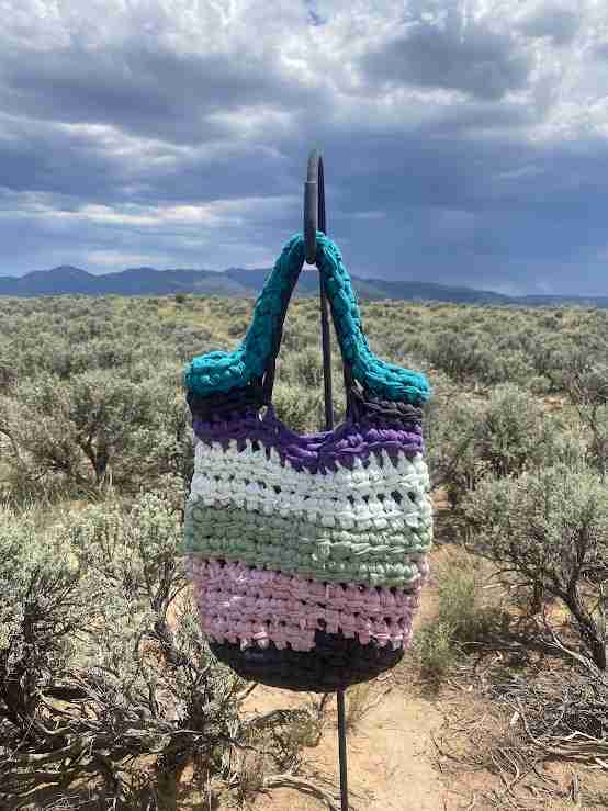 a crocheted bag on a stand in the desert.