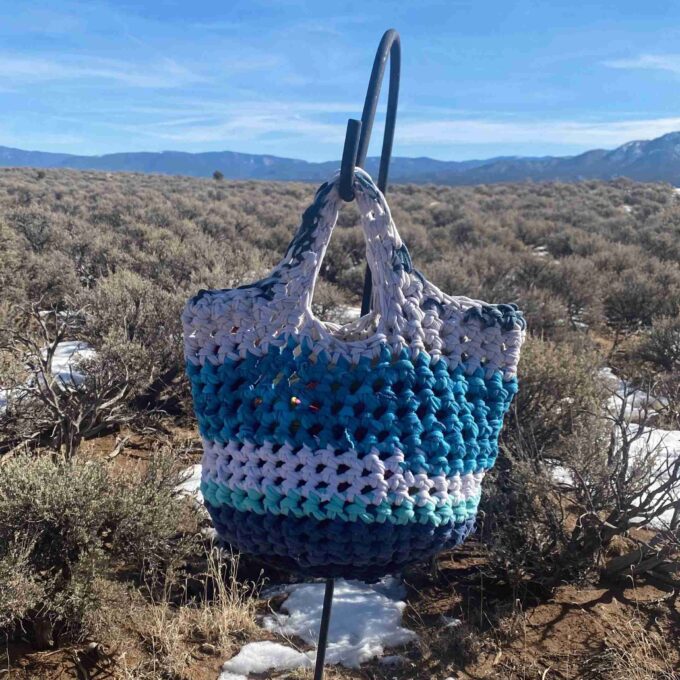 a blue and white crocheted bag sitting on top of a snow covered ground.