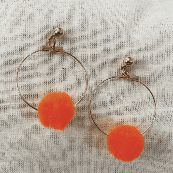 a pair of orange earrings on a white cloth.