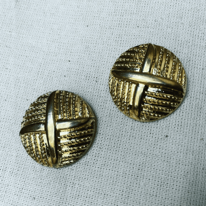 a pair of gold toned buttons sitting on top of a white cloth.
