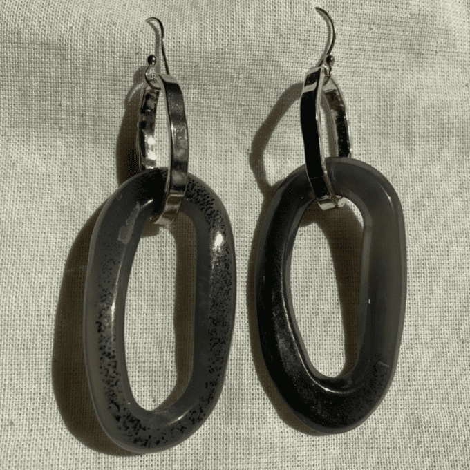 a pair of black and silver earrings sitting on top of a white cloth.