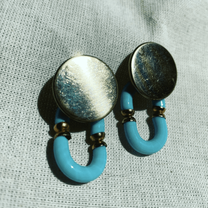 a pair of blue and gold earrings on a white cloth.