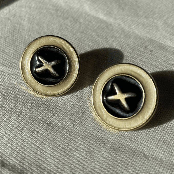 a pair of black and gold earrings on a white cloth.