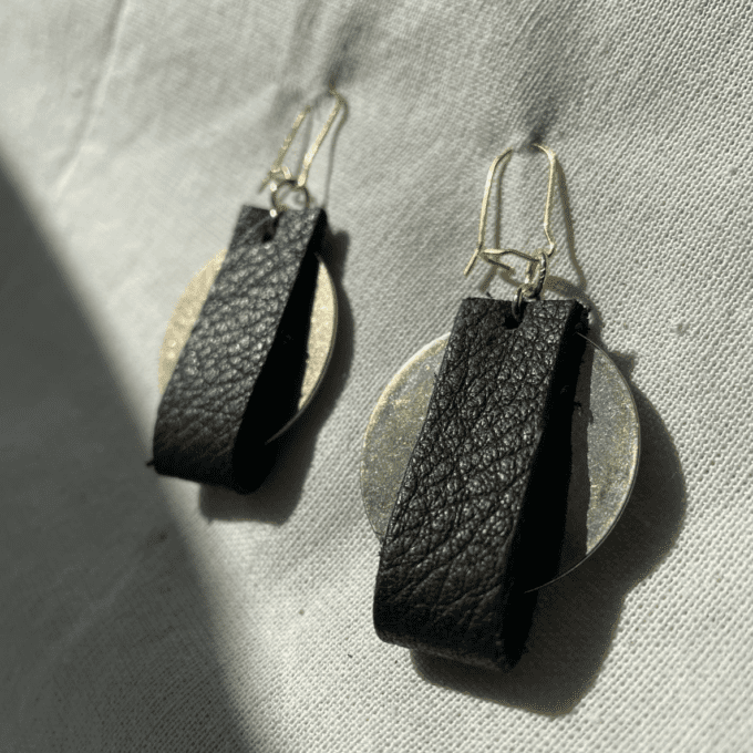 a pair of black leather earrings on a white cloth.