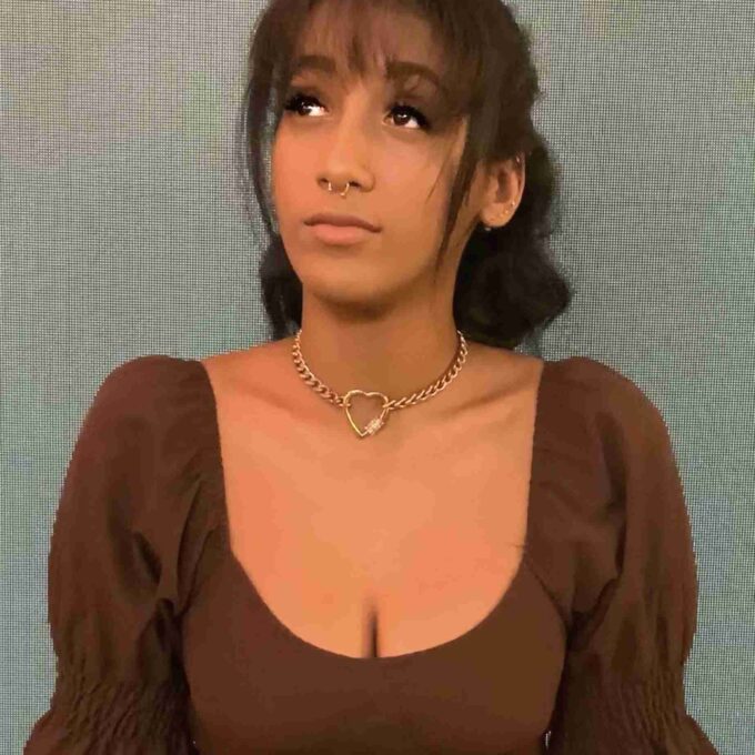 a woman wearing a brown top with a heart necklace.