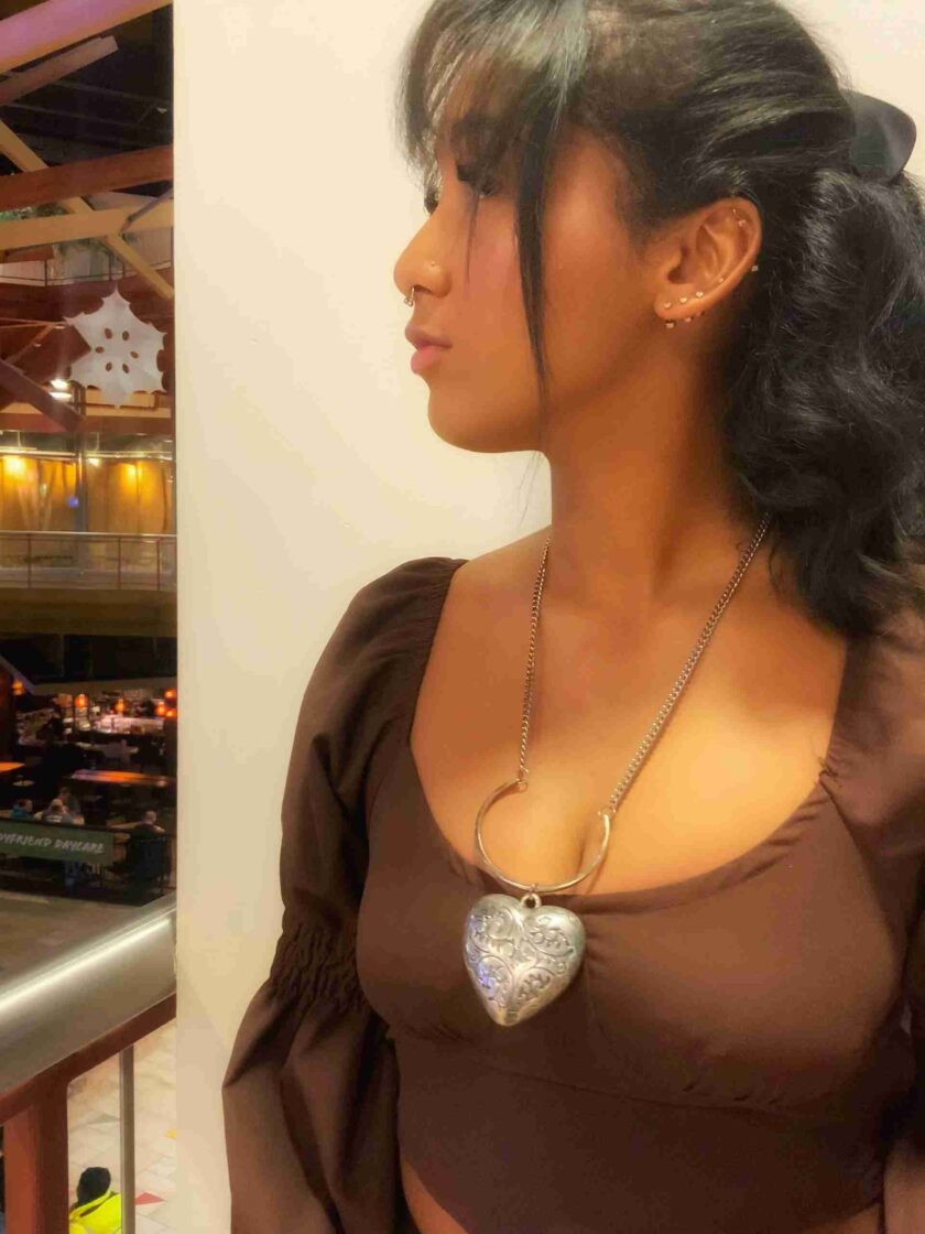 a woman wearing a brown top with a heart shaped pendant.