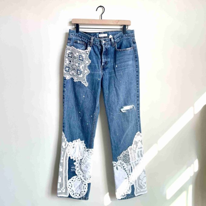 a pair of jeans with lace on them hanging on a hanger.