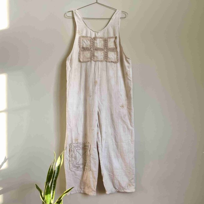 a white dress hanging on a wall next to a potted plant.