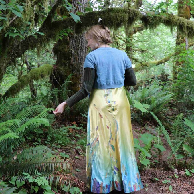 a woman in a dress walking through a forest.