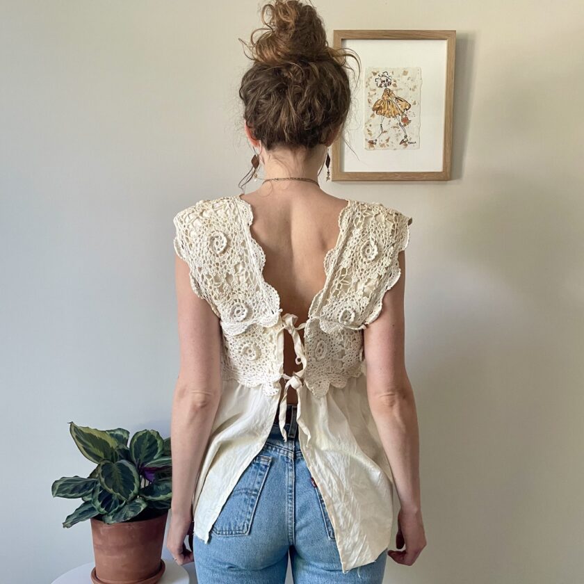 A woman standing in front of a Tea Stained Cream Crochet Festival Tank Top w/ Tie Back.
