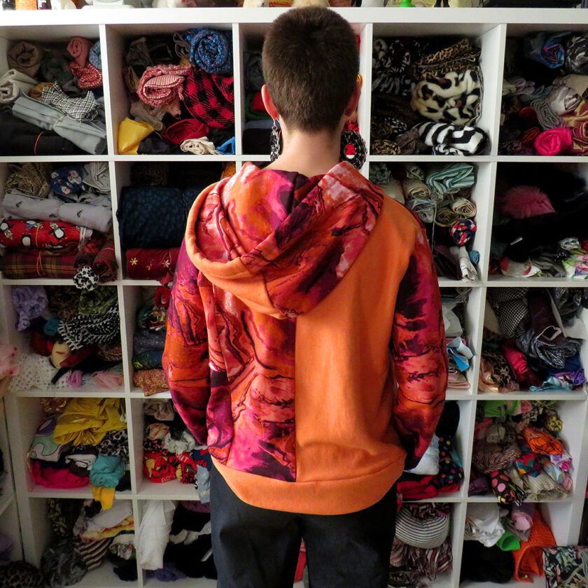 A man standing in front of a closet full of Patchwork Marbled Orange Hoodies (Small).