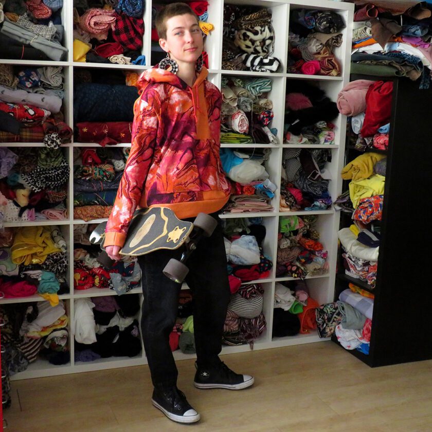 a young man holding a Patchwork Marbled Orange Hoodie (Small) in front of a closet full of clothes.