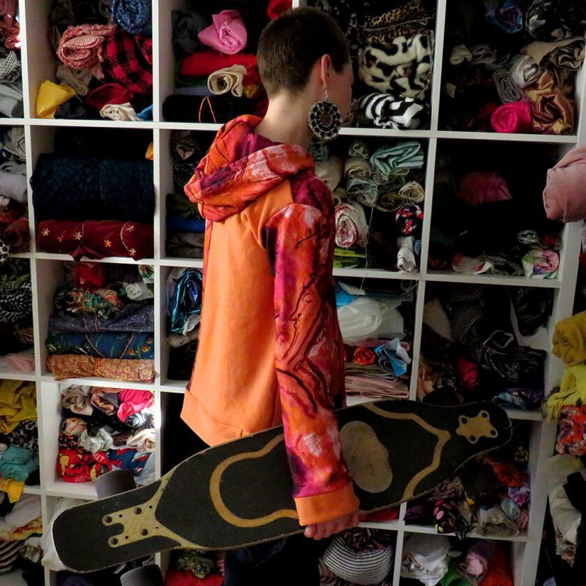 a young boy holding a Patchwork Marbled Orange Hoodie (Small) in a closet.
