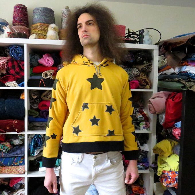 a man with long hair standing in front of a closet full of Yellow Star Hoodies (Large).