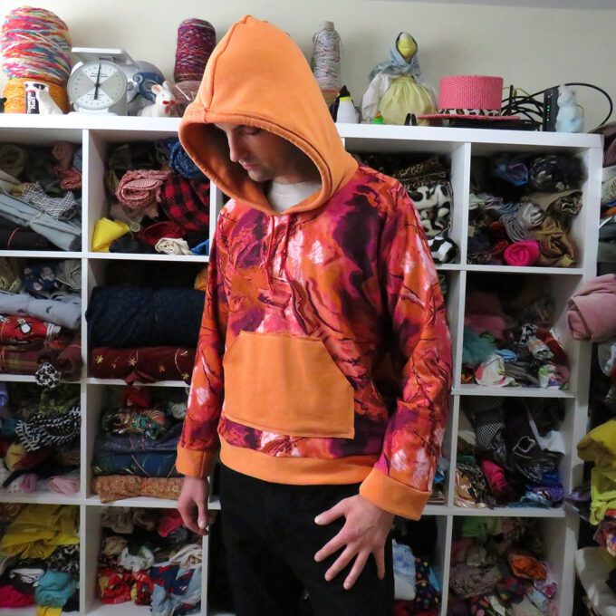 A man standing in front of a closet full of clothes, including a Marbled Orange Hoodie (X-Large).