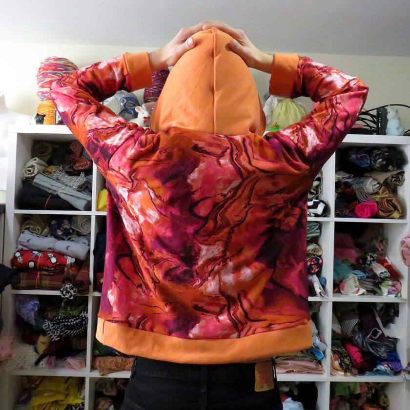a person standing in front of a Marbled Orange Hoodie (X-Large) hanging on a hanger.