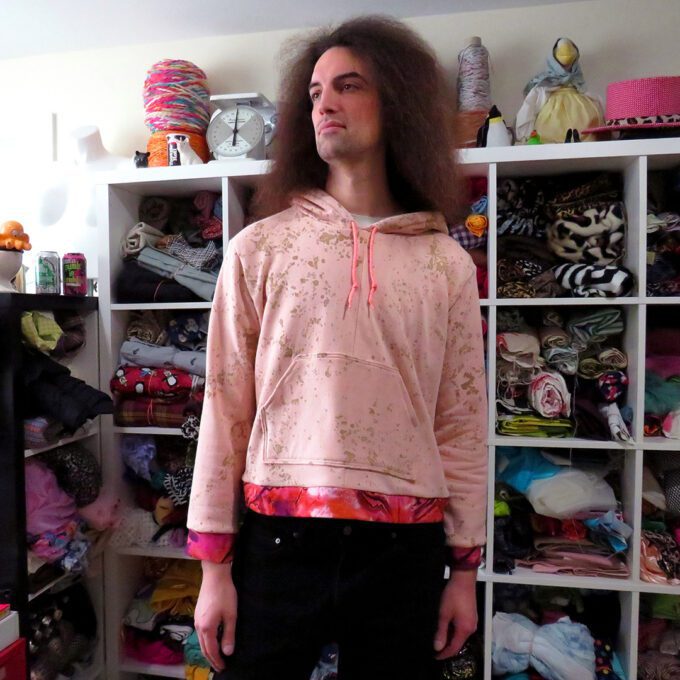 A man with long hair standing in a closet wearing a Rusty Pink Hoodie (Large).