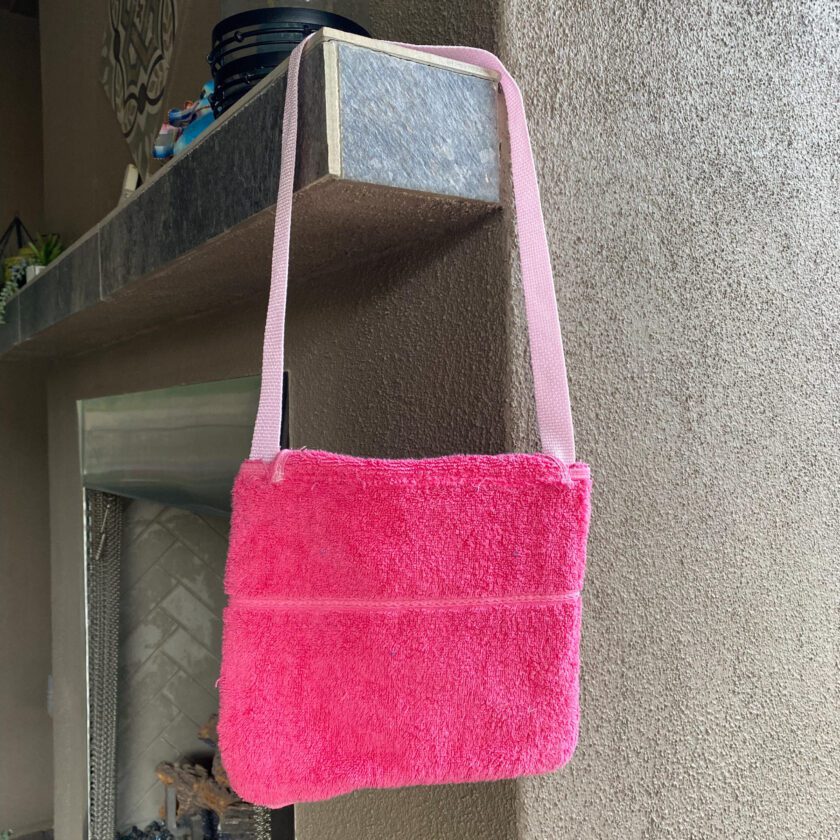 A 1of1 pink terrycloth purse hanging from a hook on a wall.
