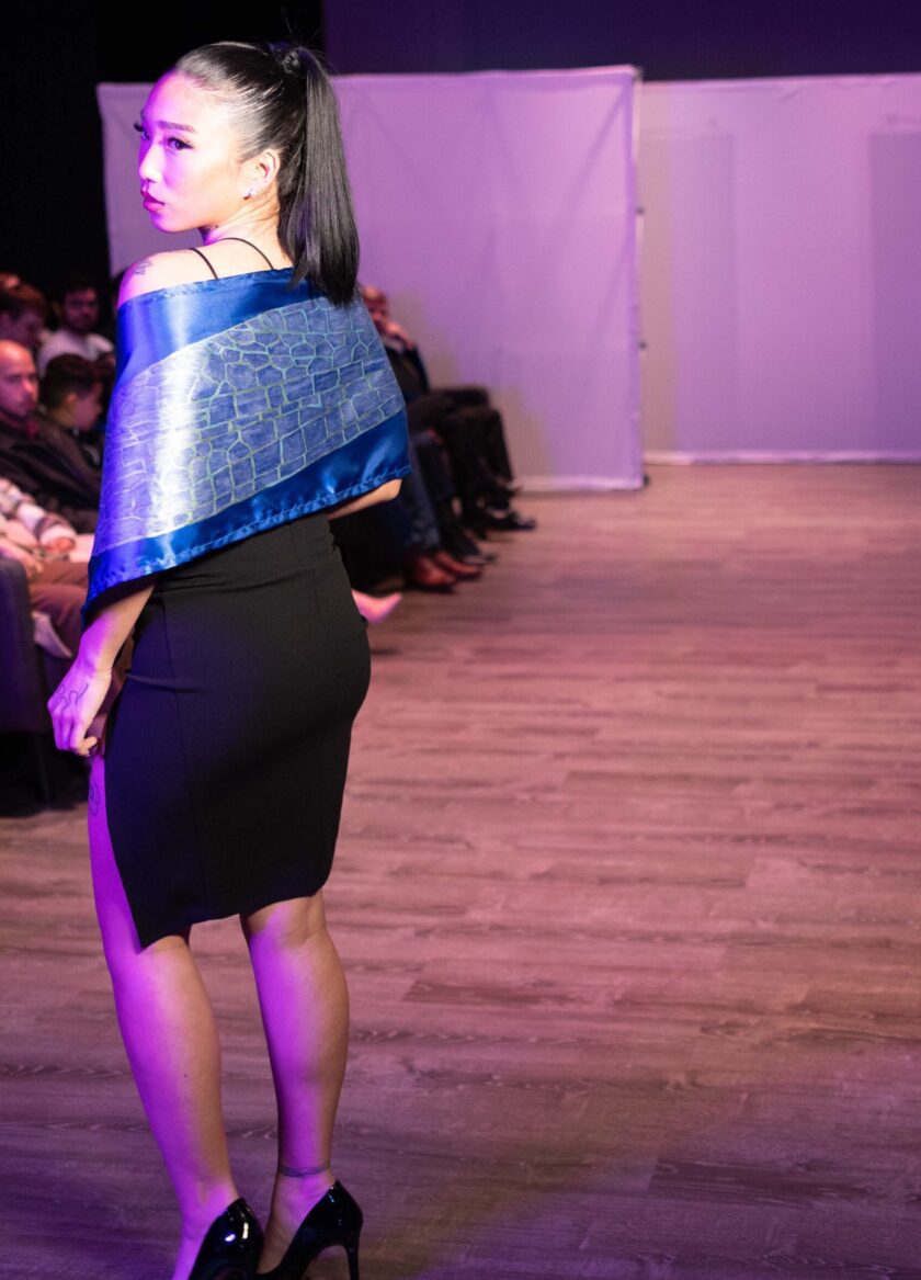 A woman in a black dress and a hand-painted iridescent blue dragonfly wing scarf jacket.