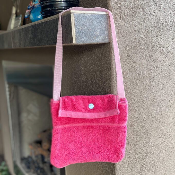 A 1of1 pink terrycloth purse hanging on the side of a building.