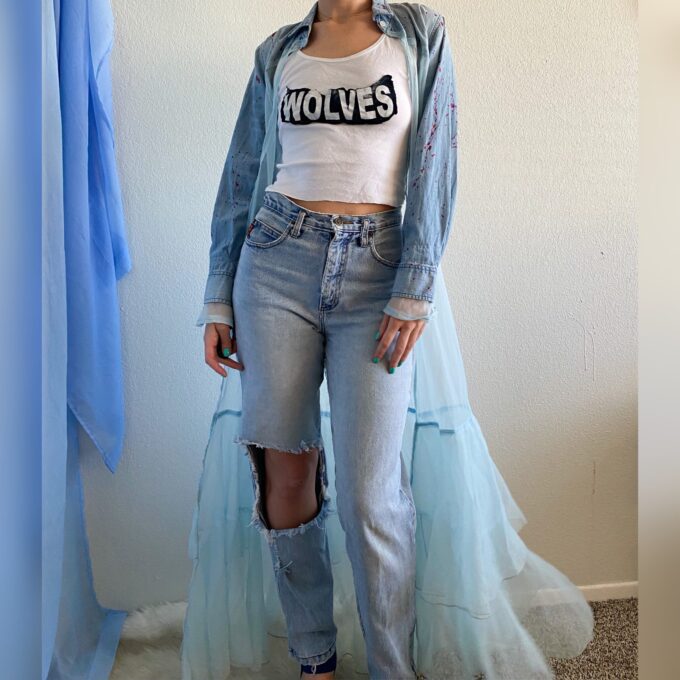 A woman standing in front of a wall wearing ripped jeans and a 1of1 fairytale feels jacket.
