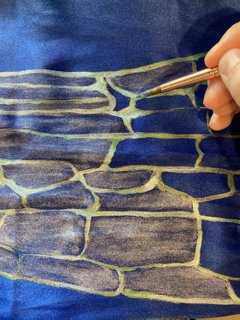 A person is drawing on a piece of paper while wearing their Hand-painted iridescent blue dragonfly wing scarf.