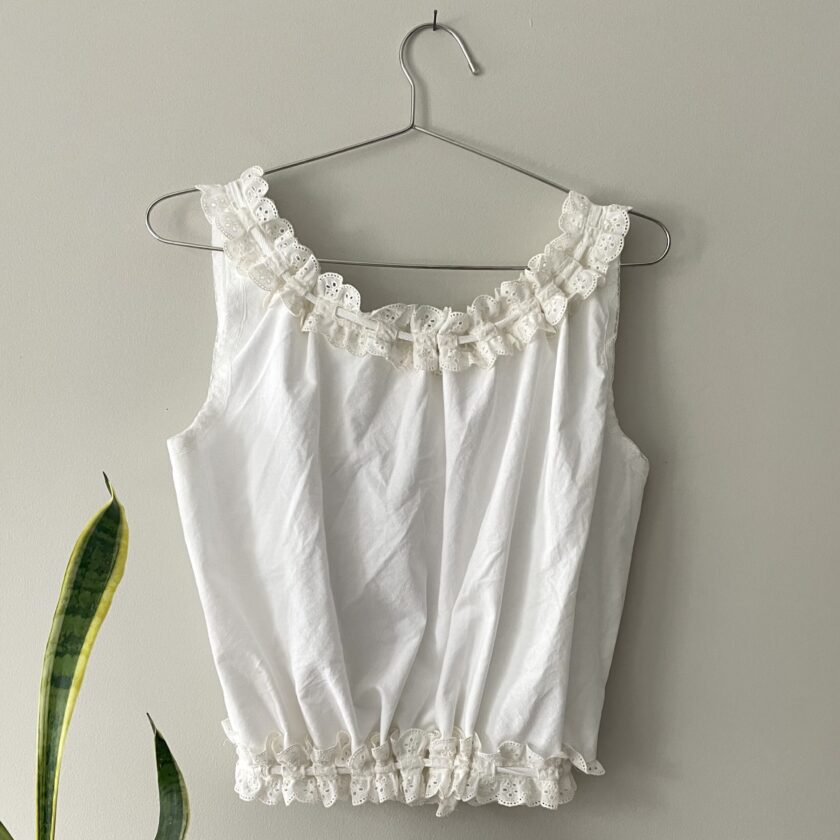 a white top hanging on a wall next to a plant.