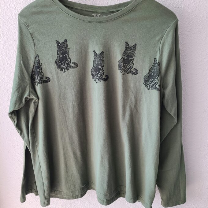 a green shirt with cats on it hanging on a wall.