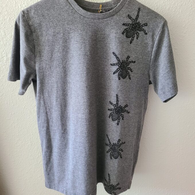 a gray t - shirt with black spiders on it.