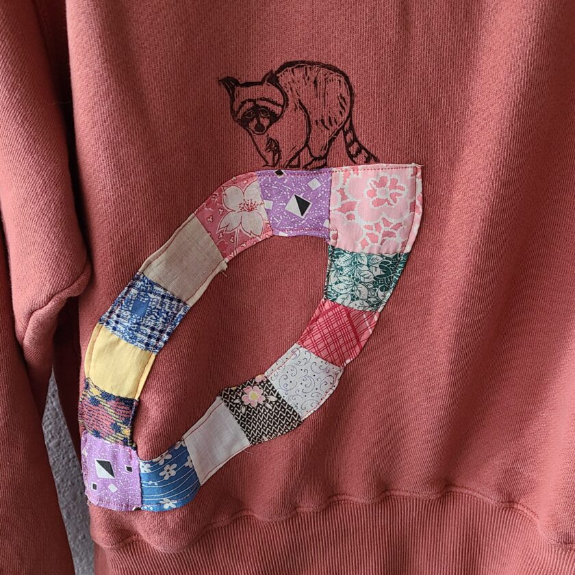 a red sweatshirt with a patchwork raccoon on it.