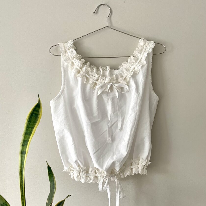 a white blouse hanging on a wall next to a potted plant.