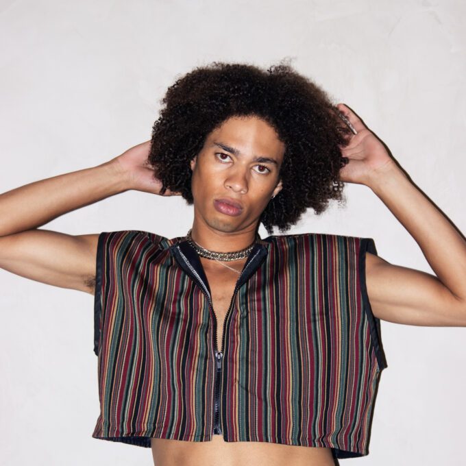 A young man in an Upcycled Sleeveless Cropped Jacket, One Size Fits Most, 1 of 1 posing with his hands on his hips.