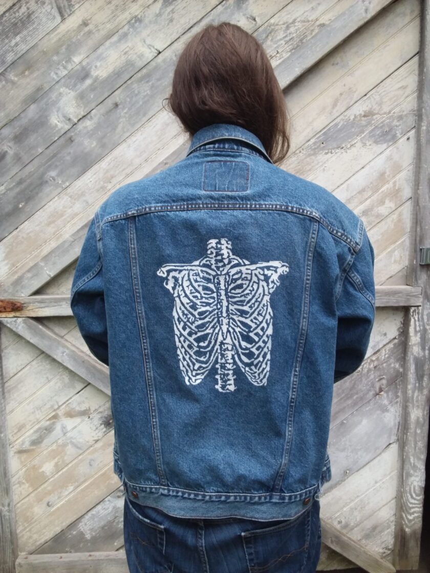 A person wearing an upcycled vintage Levi's jean jacket with a hand painted skeleton on it.