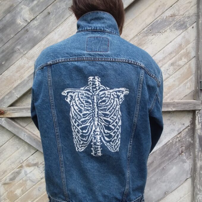 A person wearing a vintage Levi's jean jacket with a hand painted skeleton on it.