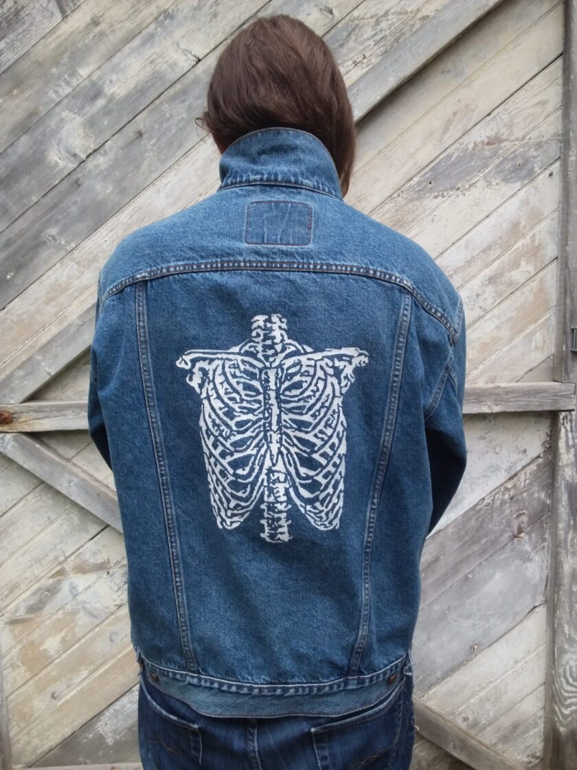 A person wearing a vintage Levi's jean jacket with a hand painted skeleton on it.