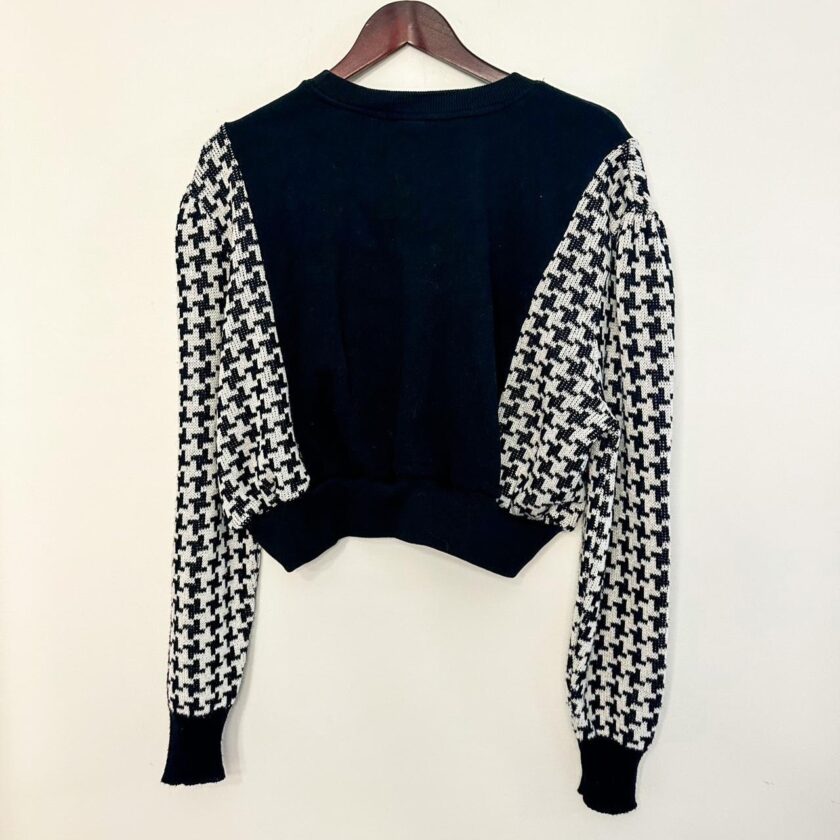 a black and white houndstooth sweater hanging on a hanger.