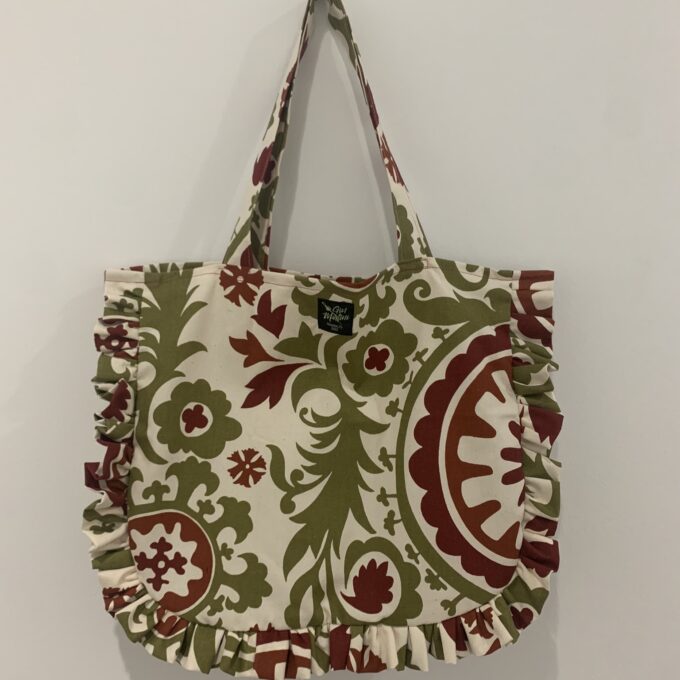 a green and red ruffled tote bag hanging on a wall.