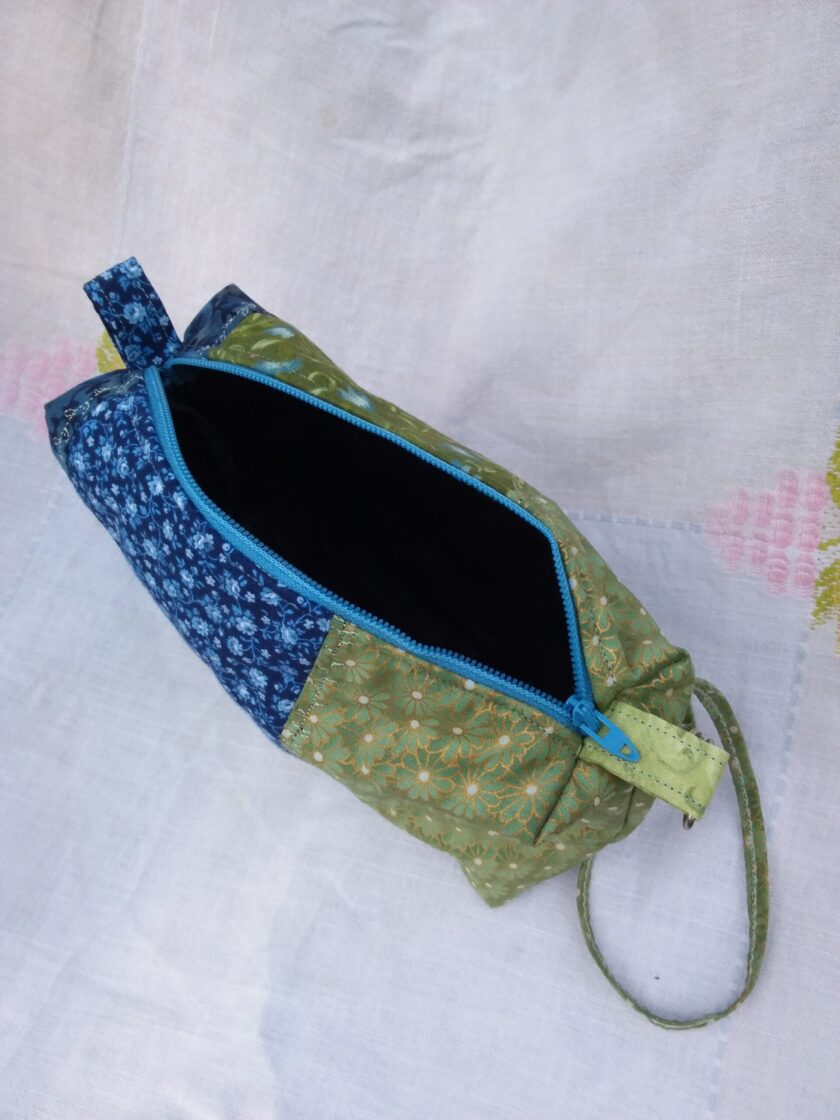 A green and blue zippered pouch made with vintage fabrics on an antique tablecloth.