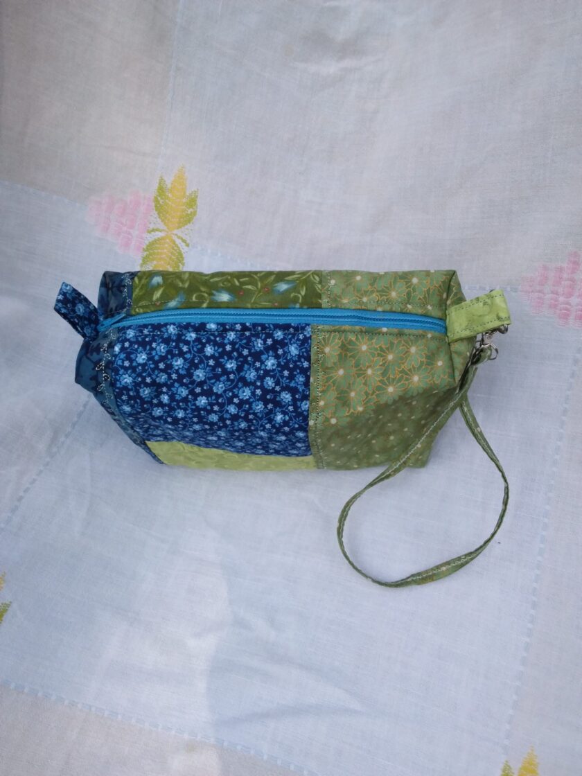 A blue and green fabric wristlet purse with a patchwork pattern in Cottage Core style.