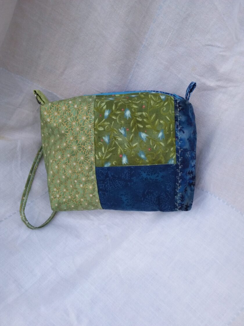 A blue and green fabric wristlet purse with a patchwork pattern in Cottage Core style.