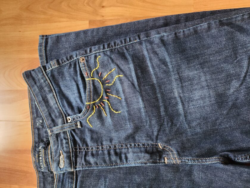 A pair of jeans with a sun embroidered on them.